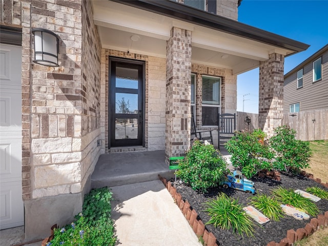 entrance to property with fence, a porch, and brick siding