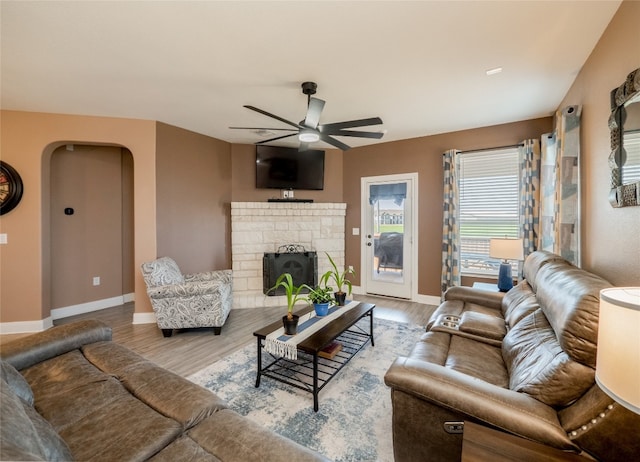 living area with a ceiling fan, arched walkways, a fireplace with raised hearth, and wood finished floors