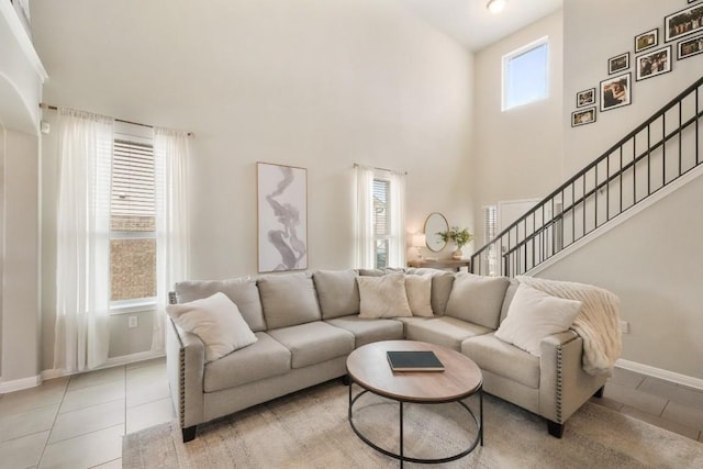 living room with a towering ceiling, baseboards, stairway, and light tile patterned flooring