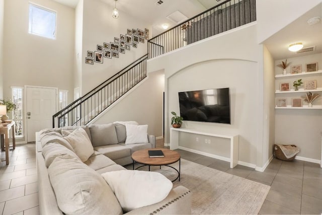 tiled living area with a towering ceiling, visible vents, stairs, and baseboards