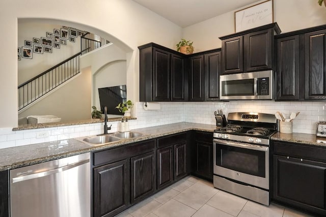 kitchen with light tile patterned floors, decorative backsplash, dark stone countertops, stainless steel appliances, and a sink