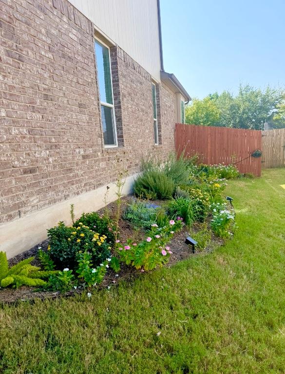 view of side of home featuring brick siding, a lawn, and fence