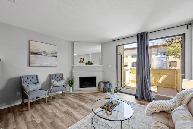 living room with a textured ceiling, wood finished floors, and a fireplace with flush hearth