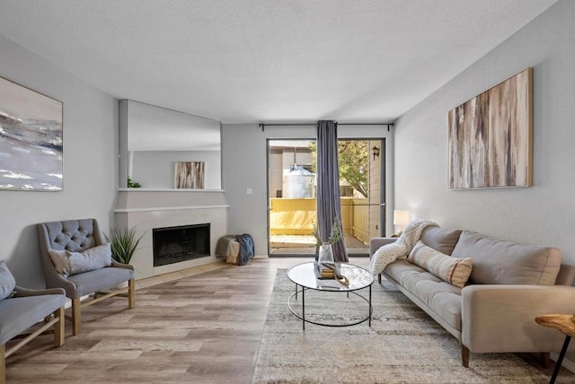 living room with a fireplace with flush hearth, a textured ceiling, and wood finished floors