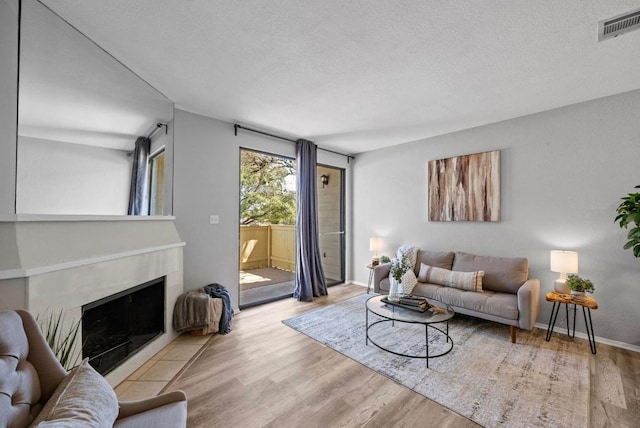 living area with a textured ceiling, wood finished floors, a fireplace with flush hearth, visible vents, and baseboards