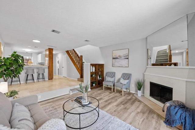 living room with baseboards, visible vents, stairs, light wood-style floors, and a fireplace