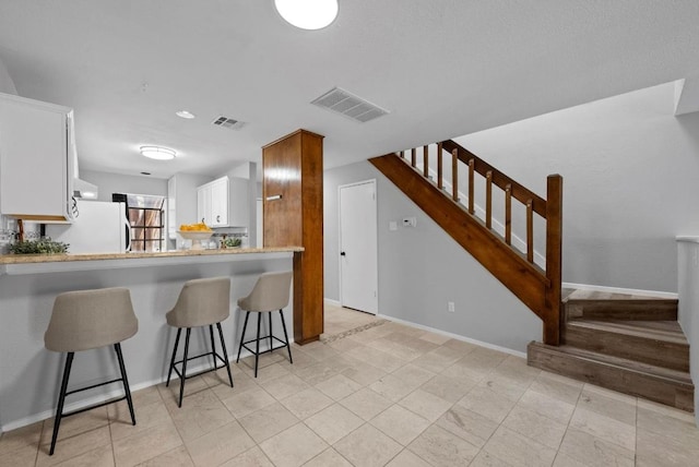 kitchen featuring a breakfast bar area, light countertops, visible vents, freestanding refrigerator, and baseboards