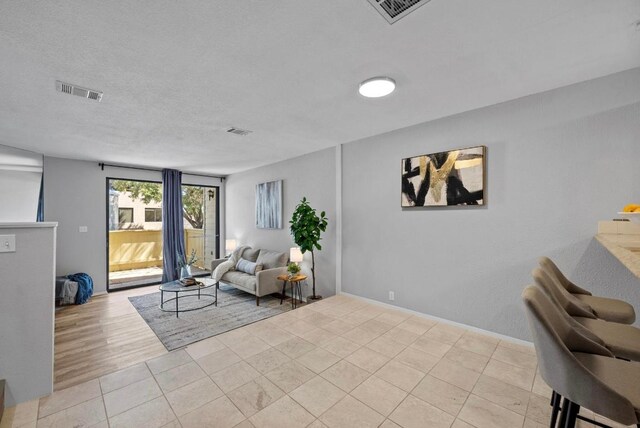 living area featuring tile patterned flooring, visible vents, and a textured ceiling