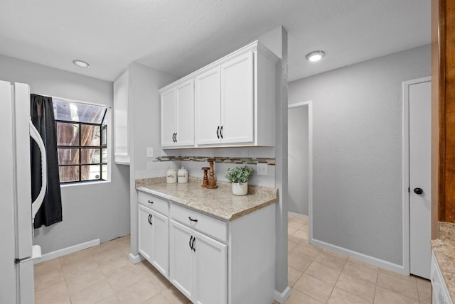 kitchen featuring light tile patterned floors, baseboards, white cabinetry, and freestanding refrigerator