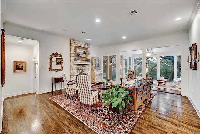 living area featuring a stone fireplace, wood finished floors, visible vents, baseboards, and ornamental molding