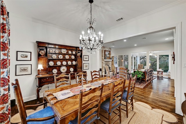 dining area with a stone fireplace, wood finished floors, visible vents, baseboards, and crown molding