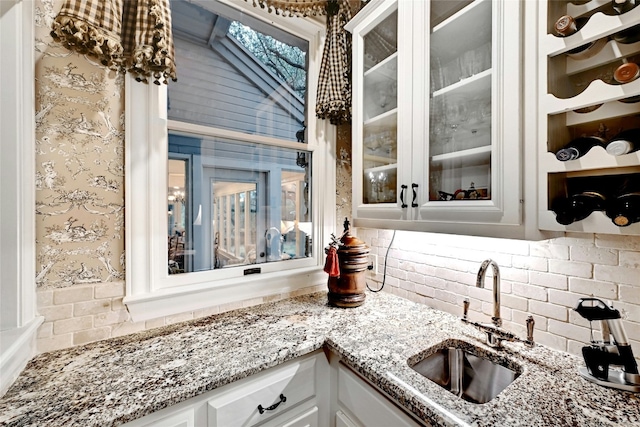 kitchen with tasteful backsplash, glass insert cabinets, white cabinetry, a sink, and light stone countertops