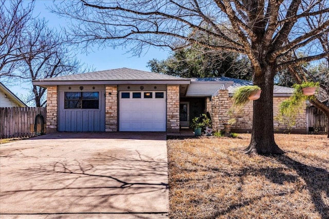 view of front of house with an attached garage, stone siding, driveway, and fence