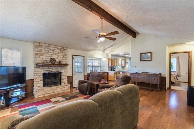 living room with lofted ceiling with beams, a ceiling fan, a stone fireplace, a textured ceiling, and wood finished floors