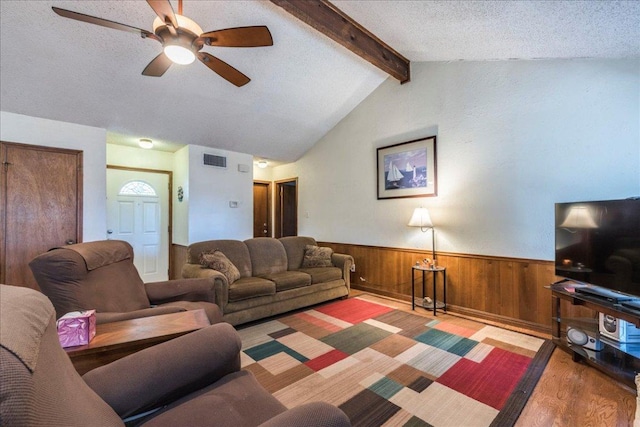 living area featuring visible vents, lofted ceiling with beams, wainscoting, wood walls, and a textured ceiling