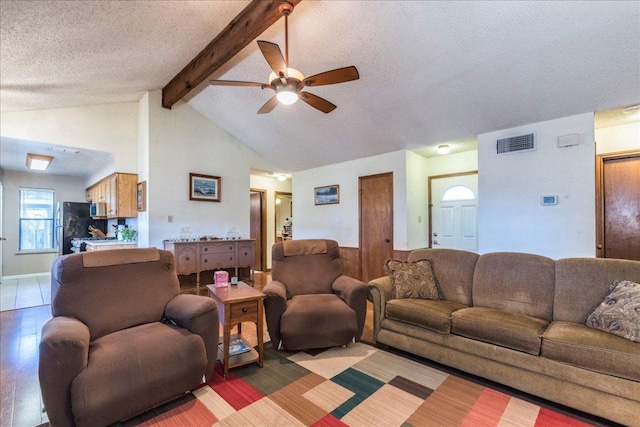 living area with beam ceiling, a wainscoted wall, visible vents, ceiling fan, and a textured ceiling