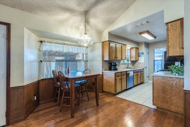 kitchen featuring dishwashing machine, light wood-style flooring, a wainscoted wall, visible vents, and brown cabinetry