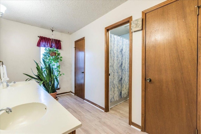 full bathroom featuring a textured ceiling, baseboards, a sink, and wood finished floors