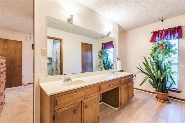 full bathroom with a textured ceiling, double vanity, wood finished floors, and a sink