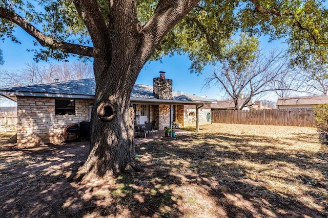 rear view of property with stone siding, a chimney, a patio, and fence private yard