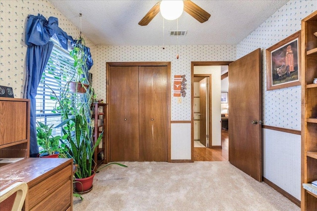 bedroom with a textured ceiling, visible vents, light colored carpet, and wallpapered walls