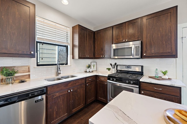 kitchen featuring dark brown cabinetry, decorative backsplash, dark wood-style floors, stainless steel appliances, and a sink