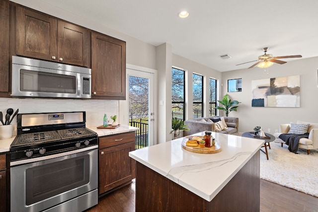 kitchen featuring appliances with stainless steel finishes, open floor plan, dark wood finished floors, and decorative backsplash