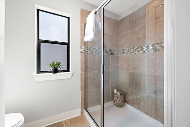 bathroom with toilet, a shower stall, and baseboards