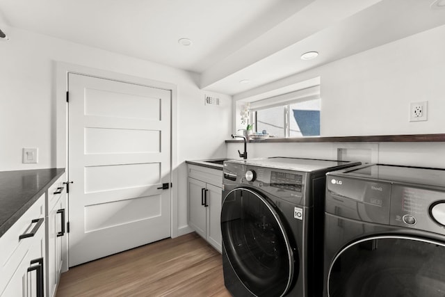 laundry room featuring separate washer and dryer, a sink, visible vents, light wood-style floors, and cabinet space