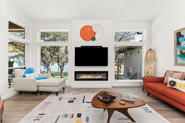 living area with plenty of natural light, wood finished floors, and a glass covered fireplace