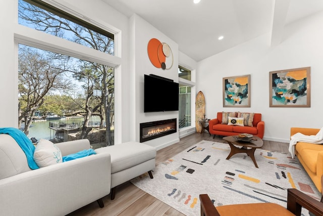 living room featuring high vaulted ceiling, recessed lighting, wood finished floors, baseboards, and a glass covered fireplace