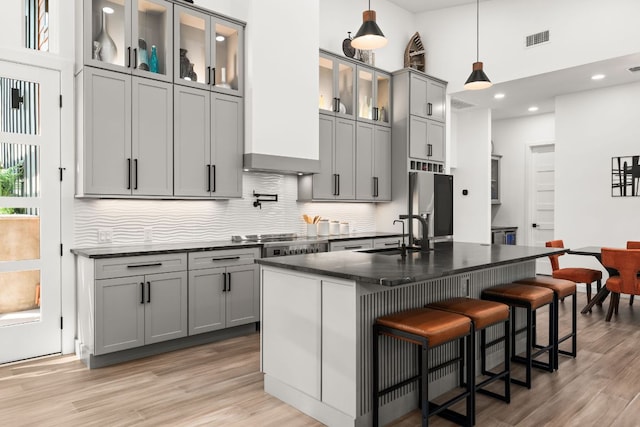 kitchen with light wood-style flooring, a sink, freestanding refrigerator, stainless steel cooktop, and dark countertops