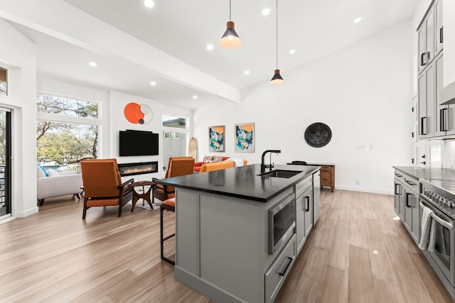 kitchen with stainless steel appliances, dark countertops, gray cabinetry, a glass covered fireplace, and a sink