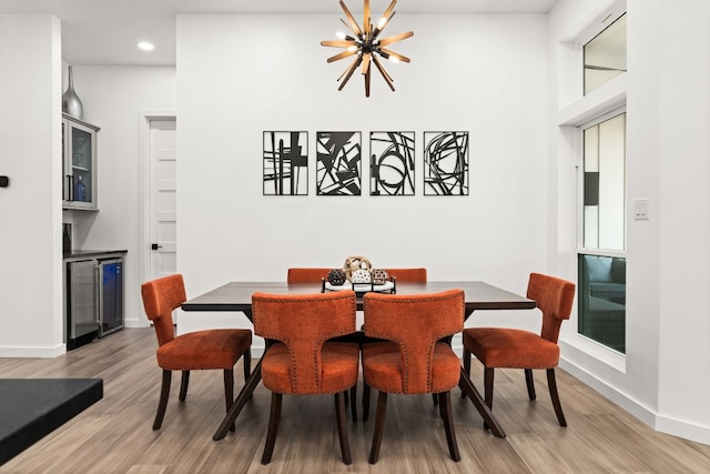 dining space with wine cooler, baseboards, light wood finished floors, and an inviting chandelier