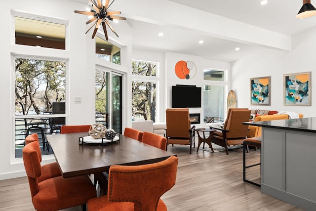 dining space featuring beam ceiling, recessed lighting, light wood-style floors, a glass covered fireplace, and a chandelier