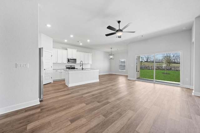 unfurnished living room with light wood-style flooring, recessed lighting, a sink, a ceiling fan, and baseboards