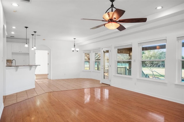 unfurnished living room featuring arched walkways, plenty of natural light, light wood-style flooring, and ceiling fan with notable chandelier