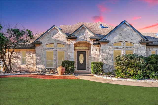 french country inspired facade featuring a front yard, stone siding, and a shingled roof