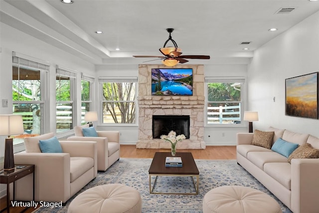 living area with visible vents, plenty of natural light, a stone fireplace, and wood finished floors