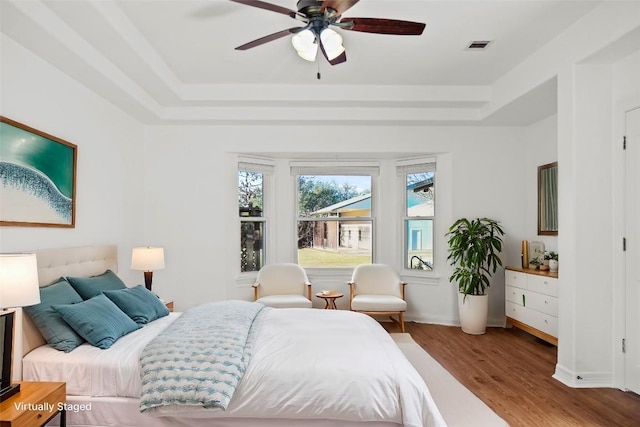 bedroom featuring visible vents, baseboards, wood finished floors, a raised ceiling, and a ceiling fan