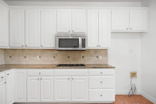 kitchen with tasteful backsplash, stainless steel appliances, white cabinets, light tile patterned floors, and light stone countertops