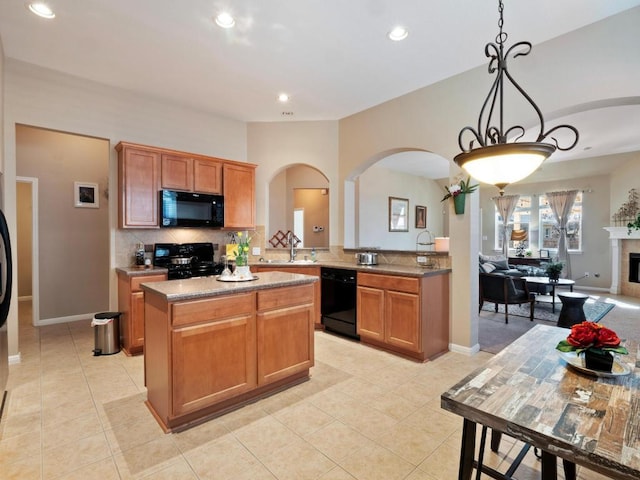 kitchen featuring a center island, backsplash, a tiled fireplace, a sink, and black appliances