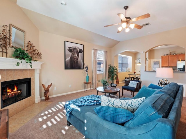 living room featuring arched walkways, lofted ceiling, a tile fireplace, visible vents, and baseboards