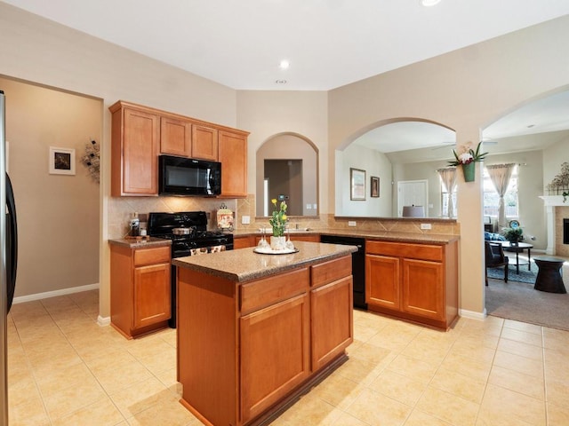 kitchen with a center island, black appliances, a fireplace, backsplash, and light tile patterned flooring