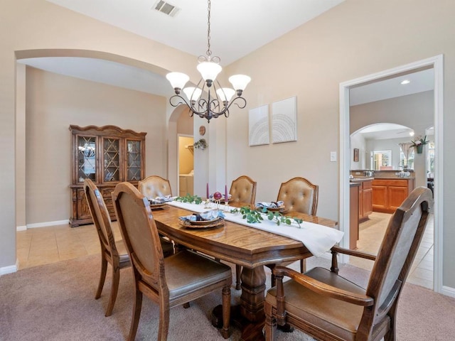 dining area with light carpet, light tile patterned floors, visible vents, arched walkways, and a chandelier