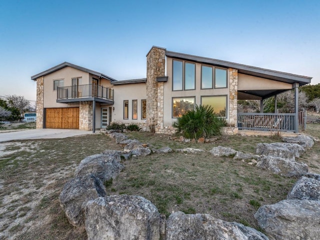 view of front of house featuring a balcony, a garage, stone siding, concrete driveway, and stucco siding