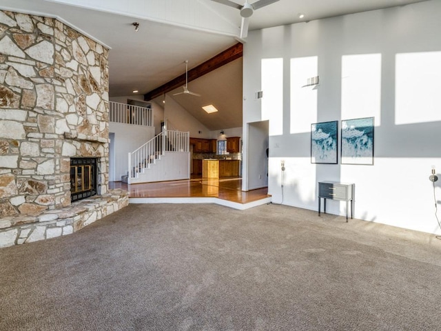 unfurnished living room featuring carpet floors, a fireplace, a ceiling fan, high vaulted ceiling, and beamed ceiling