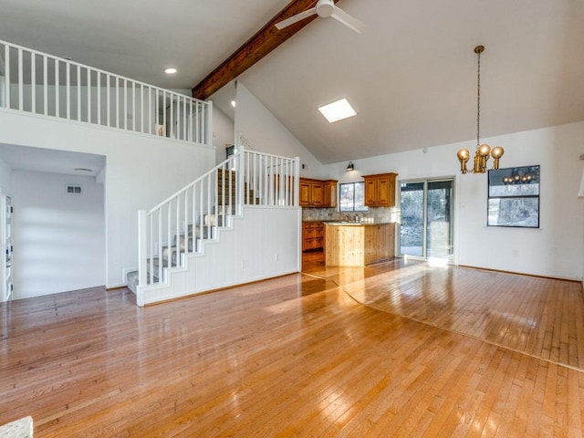 unfurnished living room with light wood-style floors, beam ceiling, high vaulted ceiling, and stairway