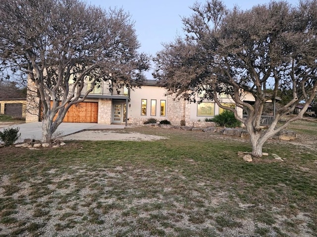 view of front facade featuring a garage, concrete driveway, stone siding, a front yard, and stucco siding