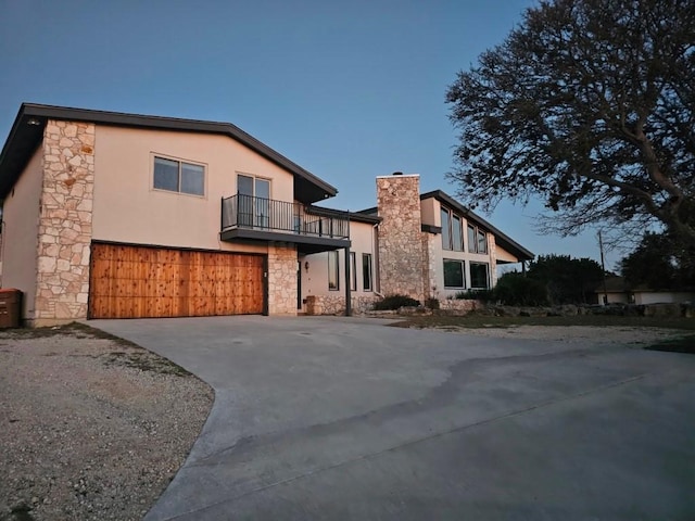 view of front of home featuring a balcony, stone siding, driveway, and stucco siding